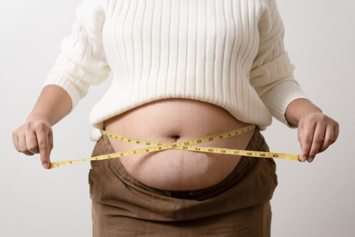 An obesity using measuring tape to show the real size. Chubby fat woman using measure tape at belly. Real size woman after gave birth to baby, real skin with wrinkles and scars.