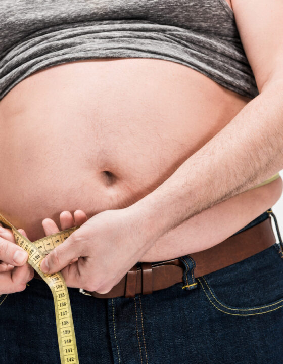 cropped view of overweight man measuring waistline with tape isolated on white