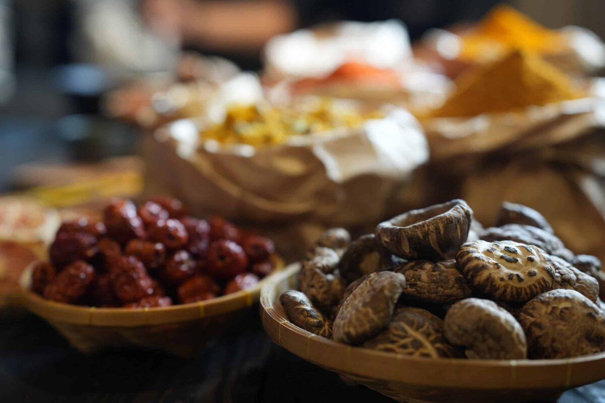 Colorful selection of dried herbs, spices, and natural ingredients in paper bags on rustic market table. Traditional Asian and herbal medicine concept.
