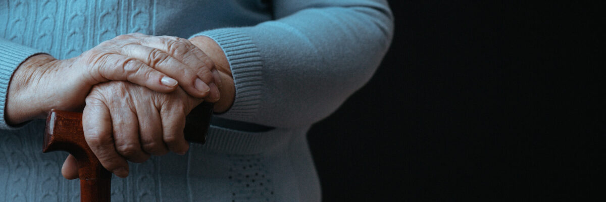 Old wrinkled woman's hands holding walking stick with dark background